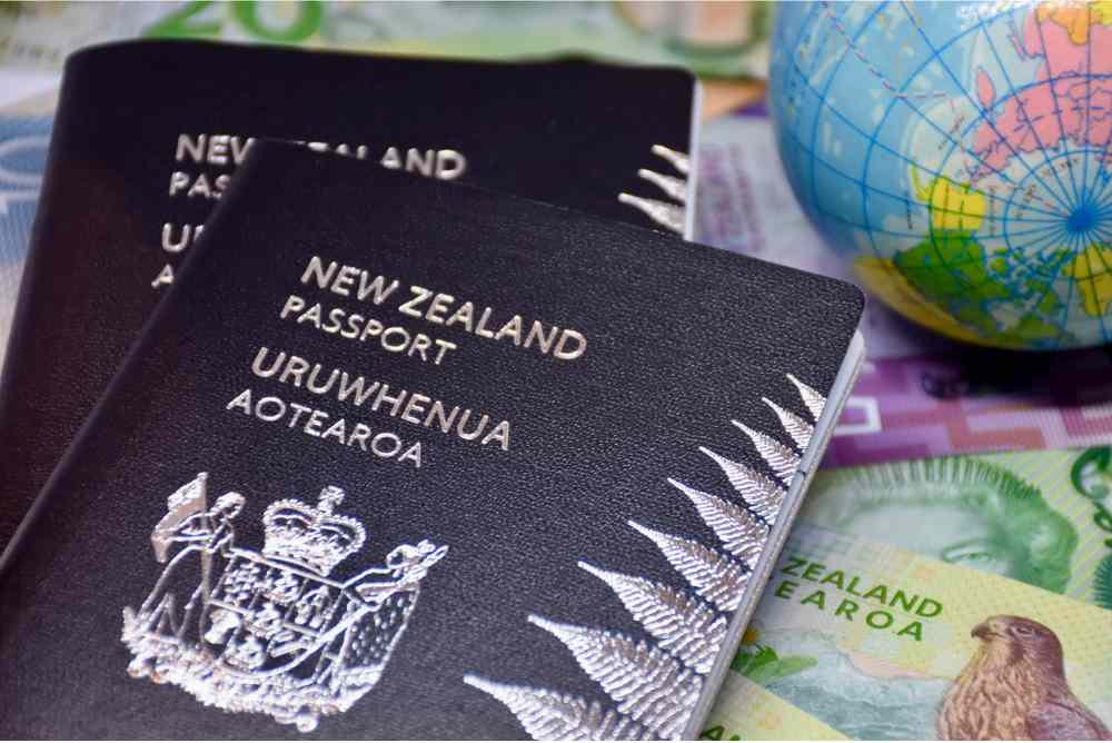 2 black and silver Aotearoa New Zealand passports sit in front of some New Zealand bank notes and a globe, to represent the immigration of Kiwi and Australian qualified lawyers overseas, and their return home.